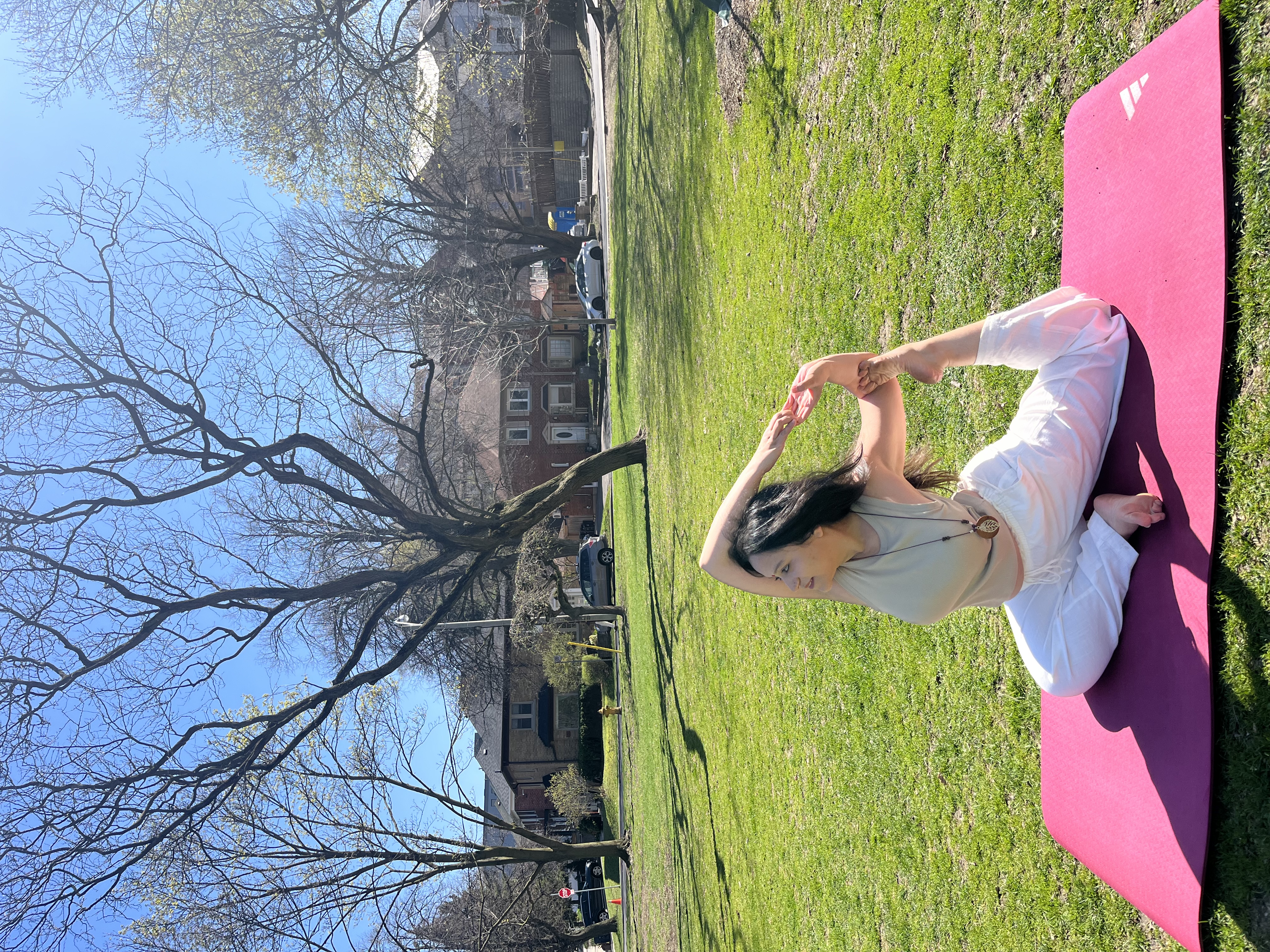 Yashna in a seated stretch on a yoga mat in a green park