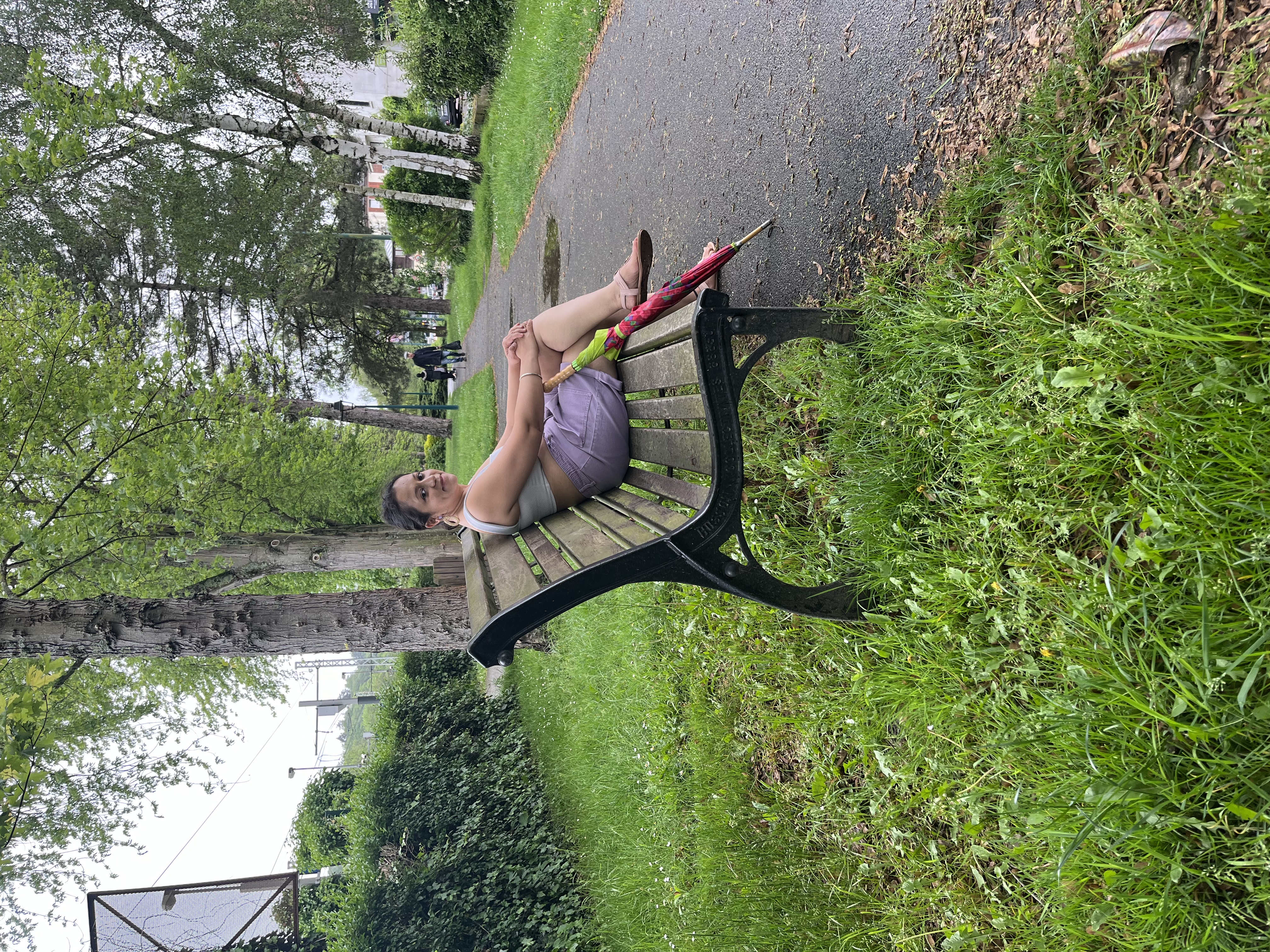 Yashna resting on a park bench with an umbrella beside her
