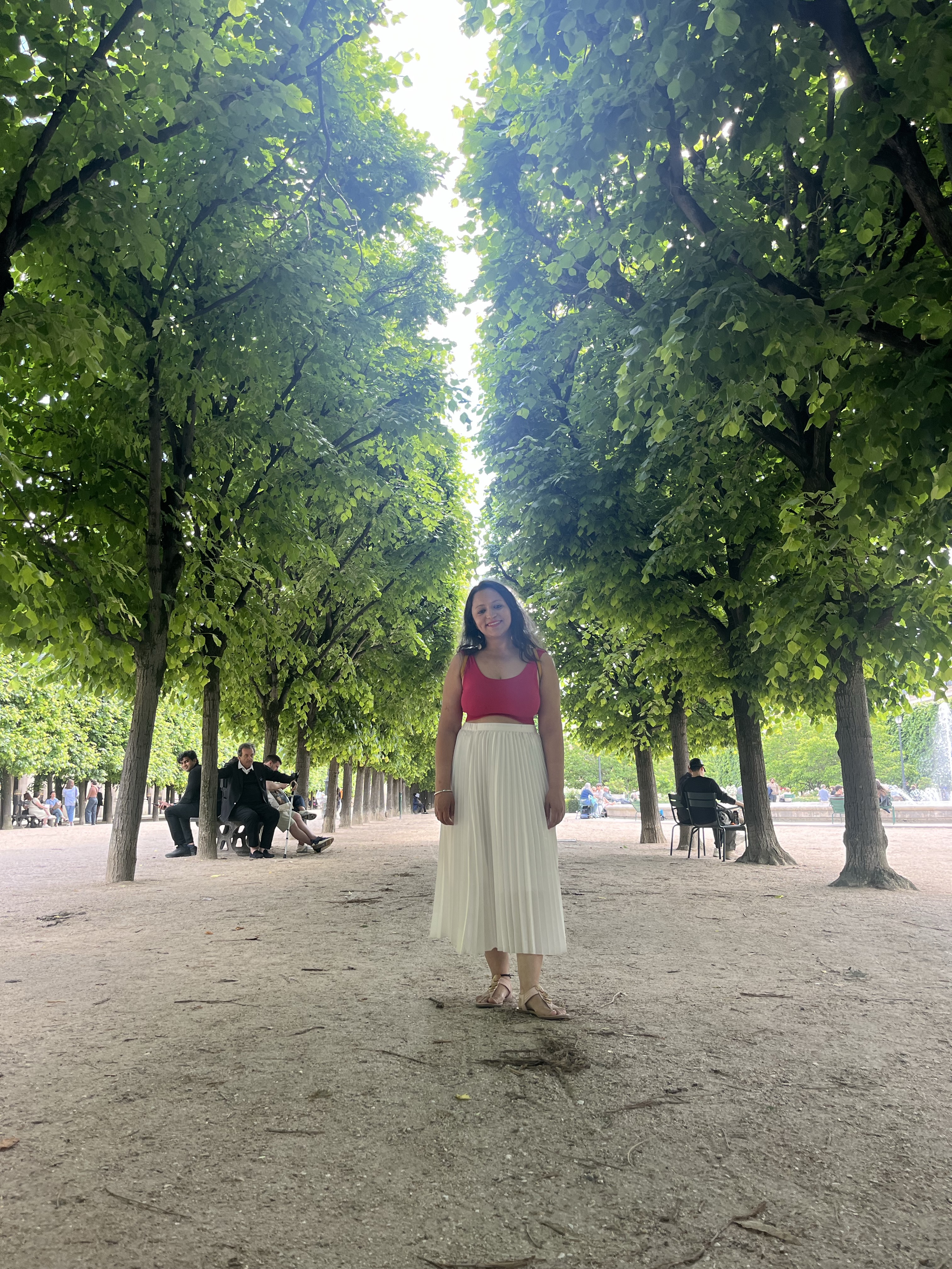 Yashna standing in a tree-lined park alley, smiling toward the camera