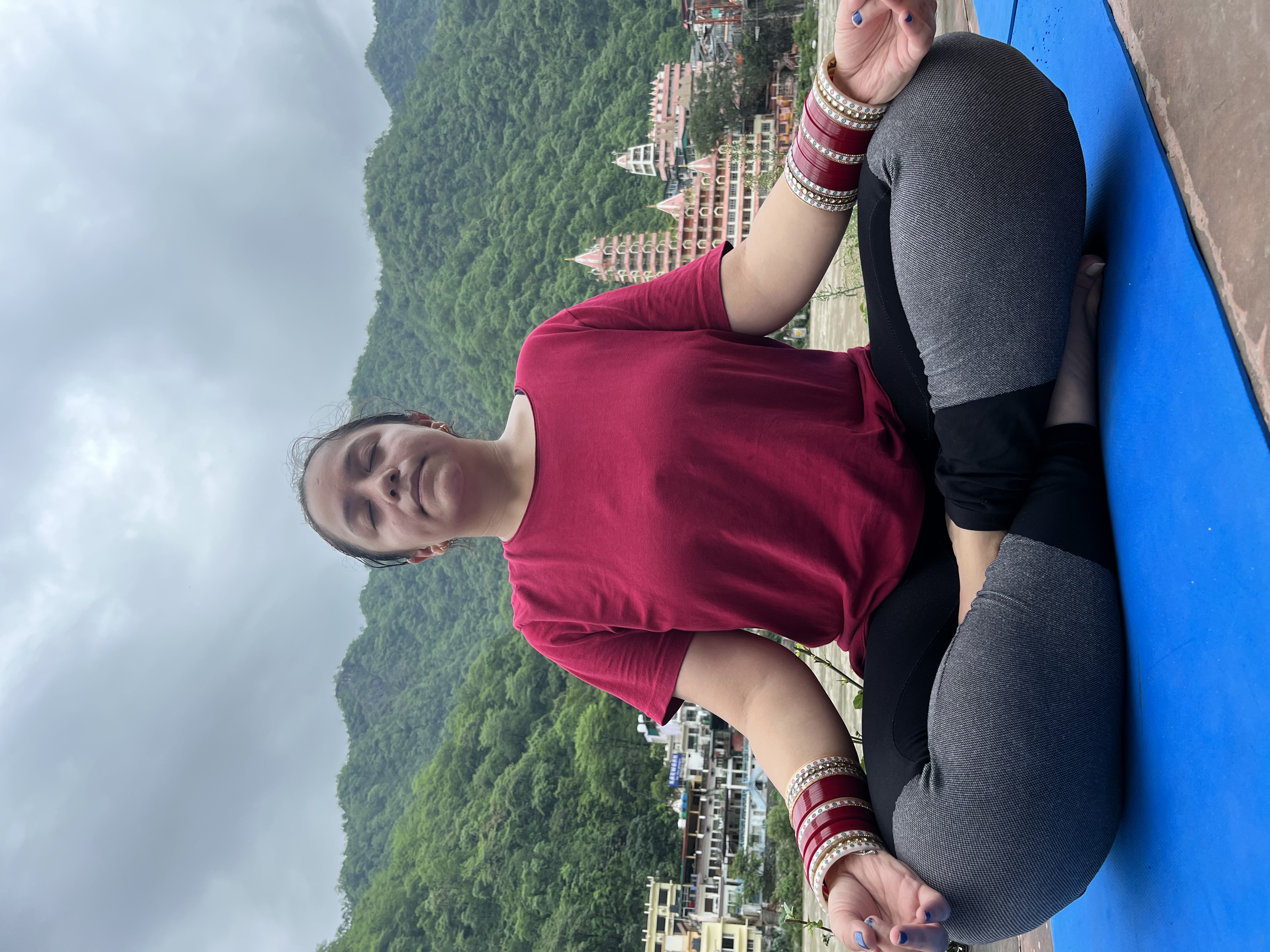Yashna meditating with eyes closed, hills and temple spires behind her