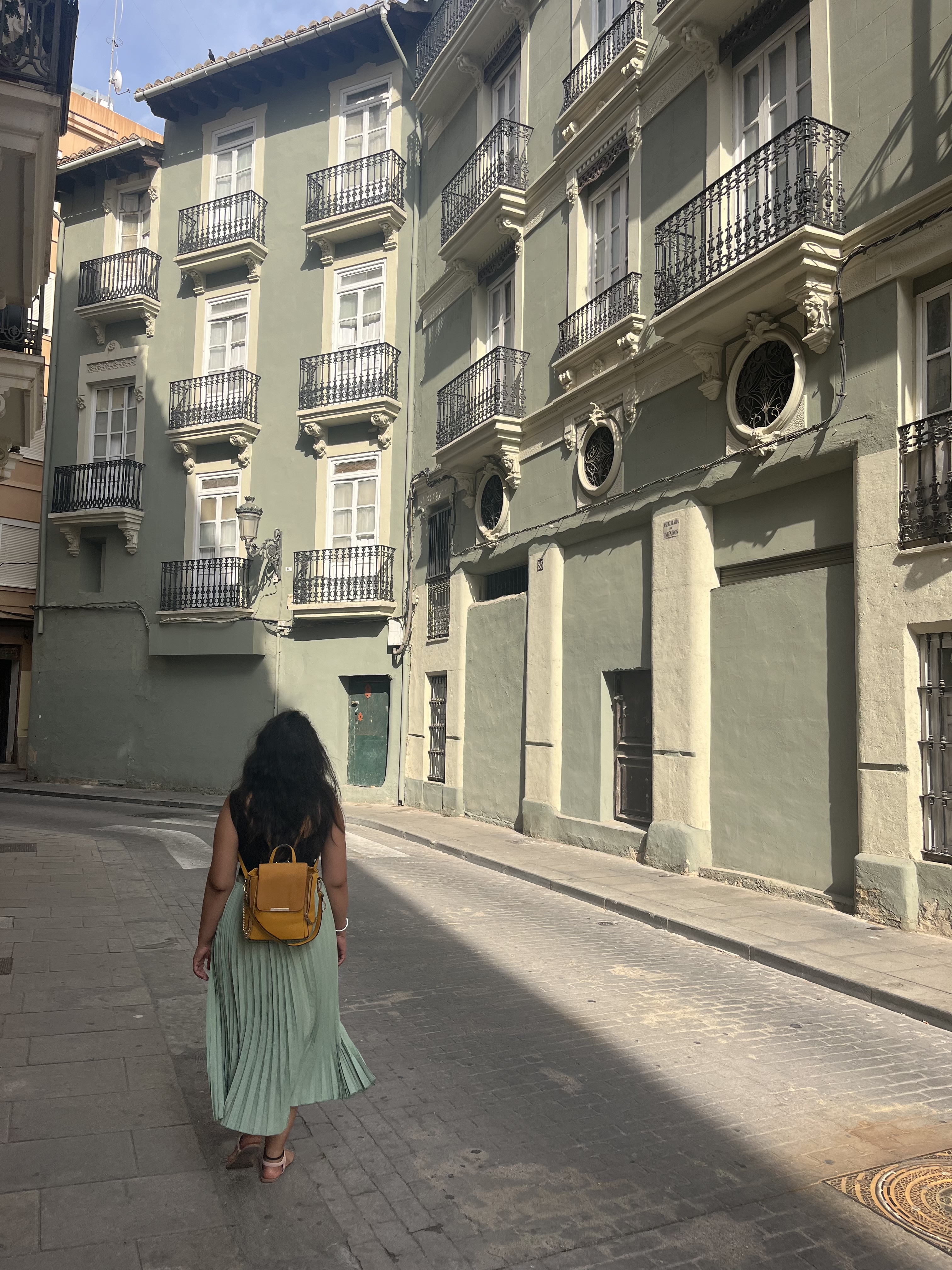 Yashna walking away down a quiet street of pale green buildings