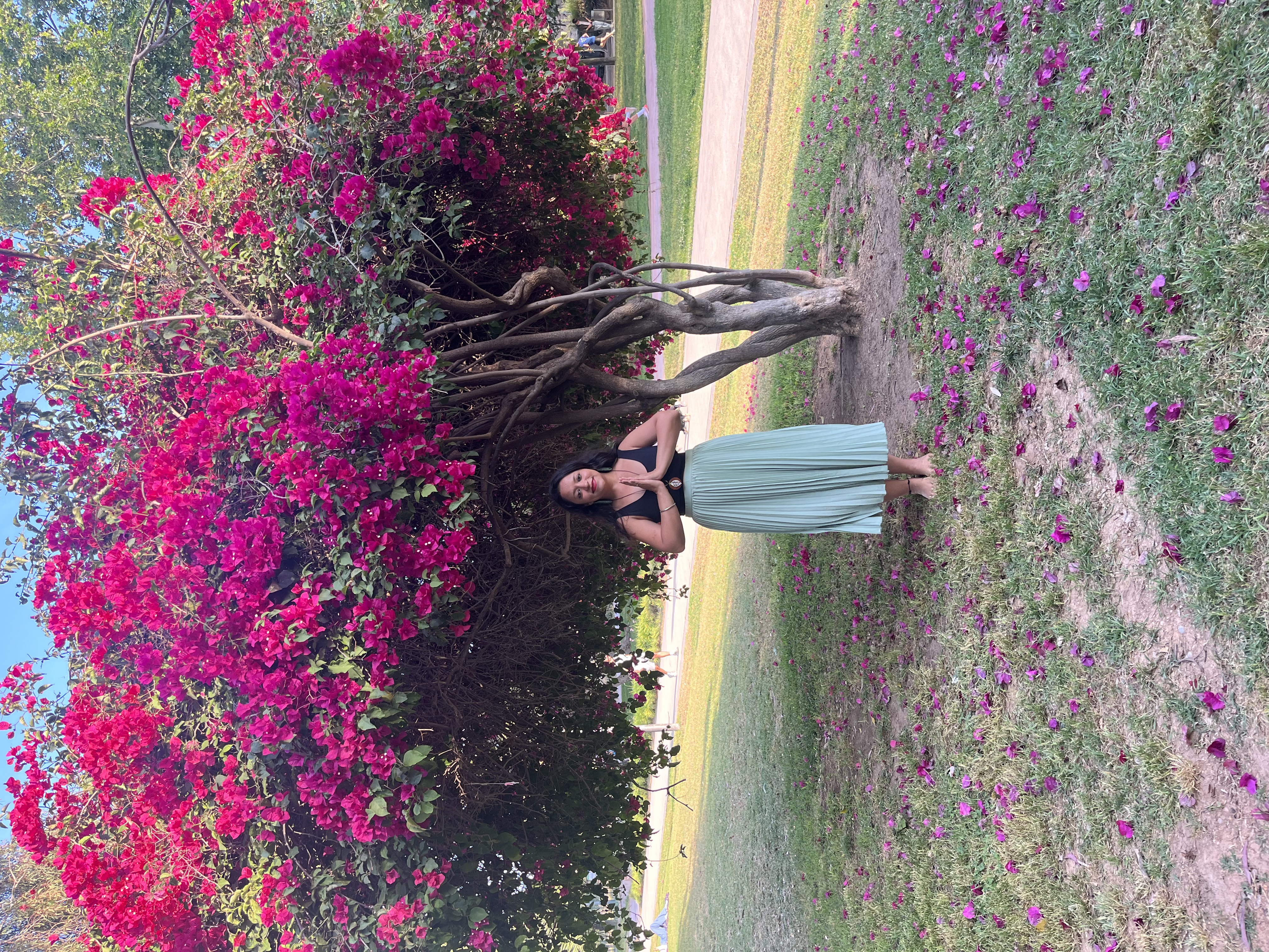 Yashna in namaste beside a large bougainvillea in bloom