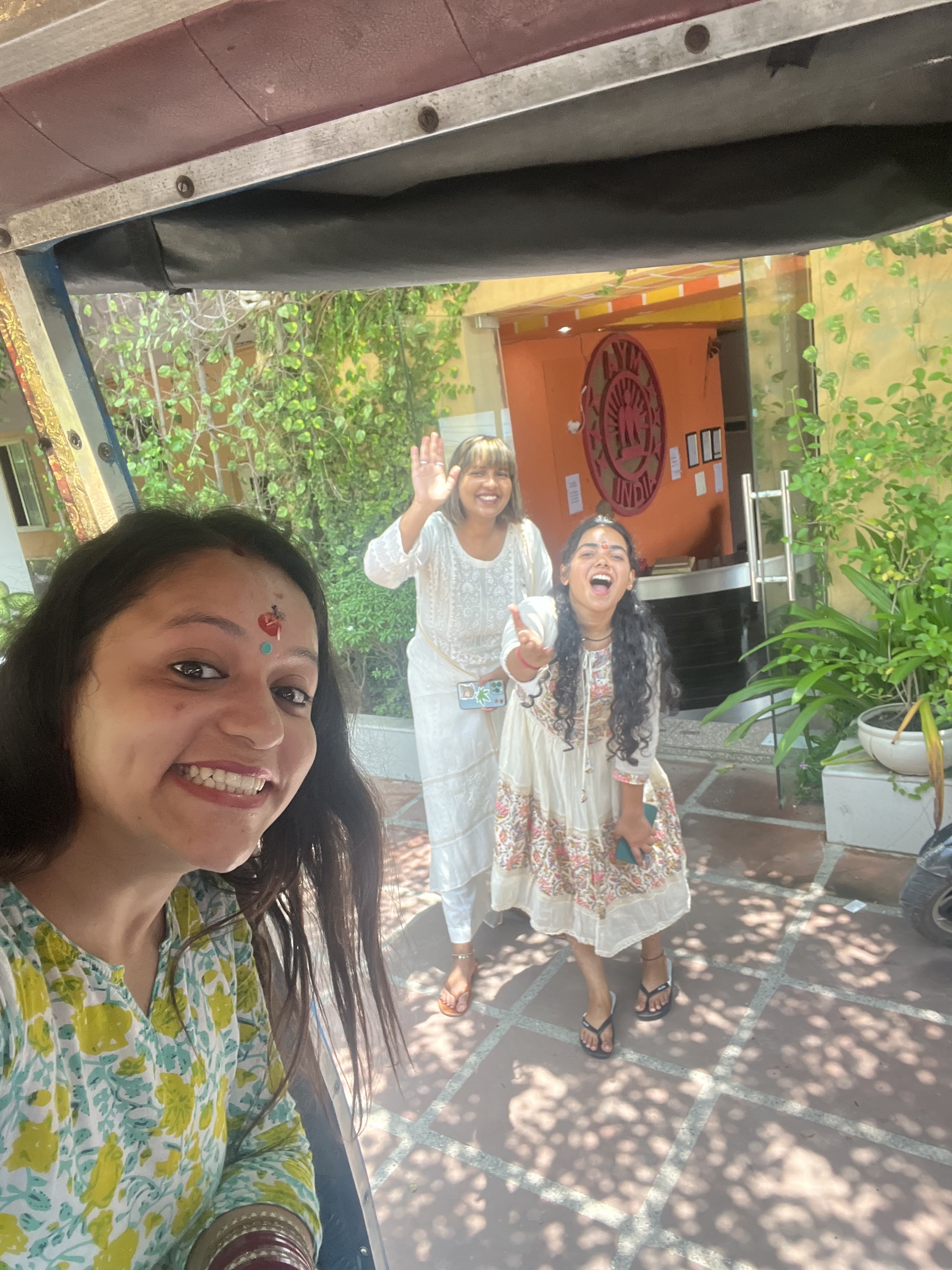 Yashna smiling from an auto rickshaw as friends wave from a yoga school entrance