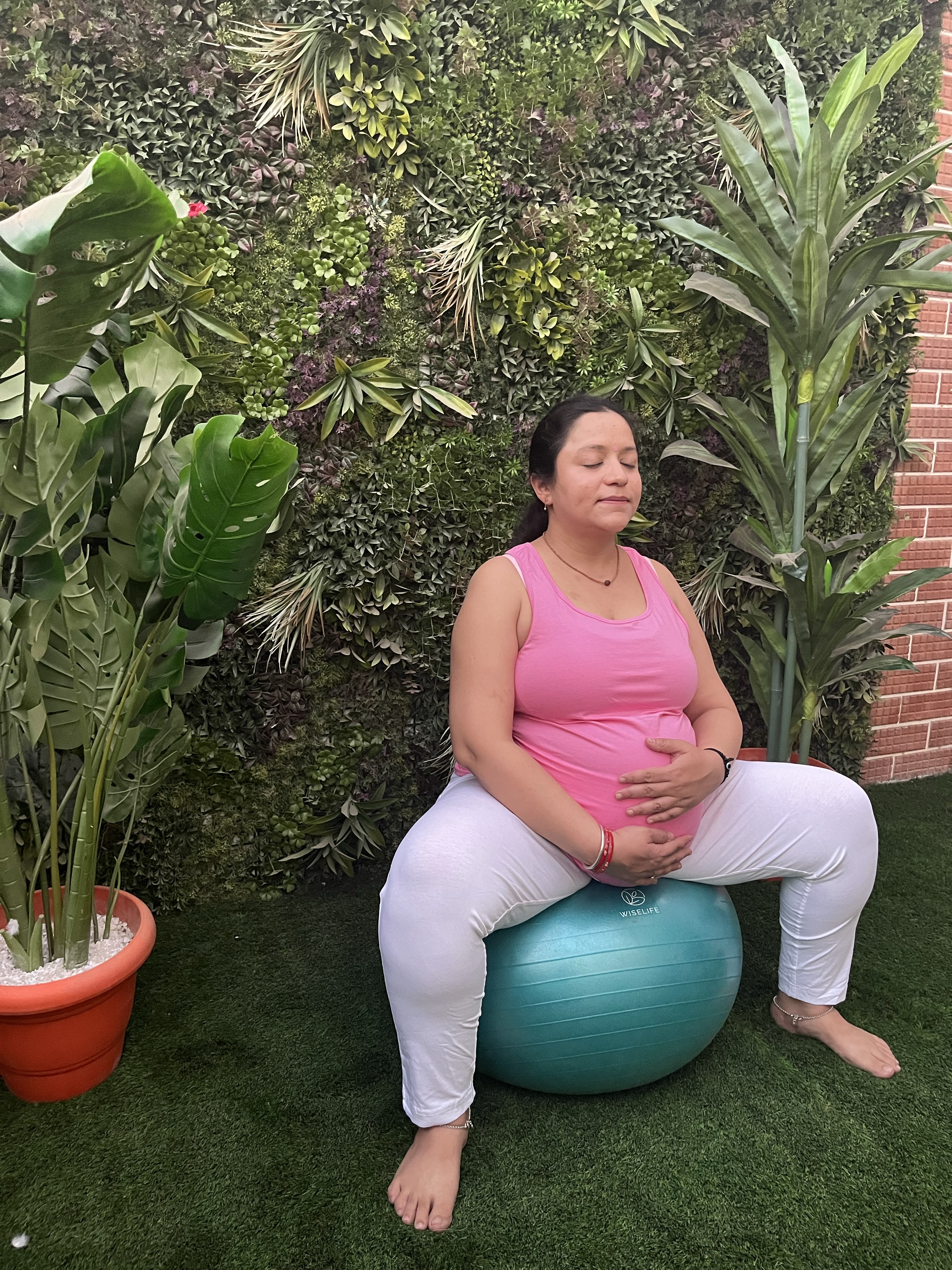 Yashna sitting on a balance ball, hands resting on her pregnancy